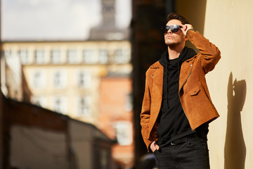 Fototapeta premium Model looking man stand near the wall and hold his glasses towards the sun shine
