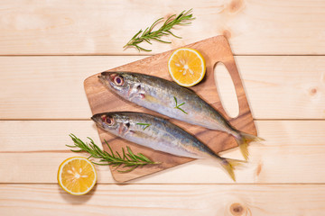Fish dish cooking with various ingredients. Fresh raw fish decorated with lemon slices and herbs on wooden table.