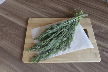 Dill bunches on chopping board on wooden background.