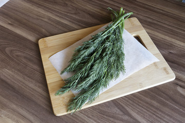 Dill bunches with red chili peppers on chopping board on wooden background.