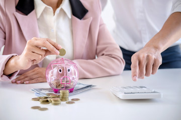 Two couples putting coins into piggy bank, writing to report and using calculator to analysis business investment strategy with income of money coin and dollar, financial concept