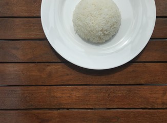 cropped shot of plain Thai rice on white plate put on brown wooden table with copy space at the bottom of frame