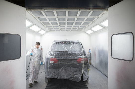 Auto painter painting a car inside a paint booth