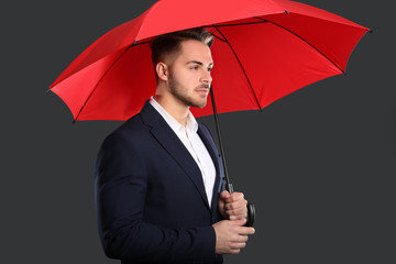 Young man in elegant suit with red umbrella on dark background