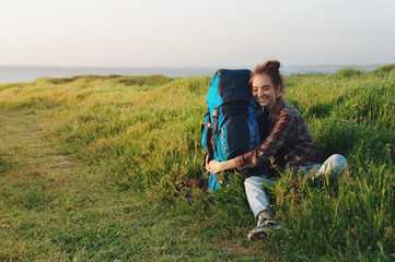 Naklejka na ściany i meble Beautiful hiker girl hugging her backpack in grass and smiling