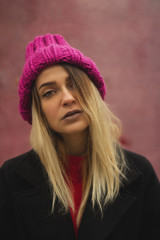  blonde girl with big eyes and plump lips against a pink background. woman in voluminous warm color fuchsia hat.