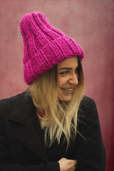  blonde girl with big eyes and plump lips against a pink background. woman in voluminous warm color fuchsia hat.