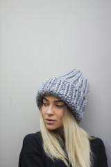 blonde girl with big eyes and plump lips against a light gray background. woman in a voluminous warm gray hat.