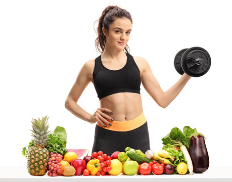 Fitness woman holding a dumbbell behind a table with fruit and vegetables