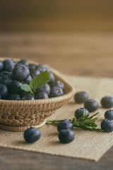 Fresh wild blueberries heap in wood basket on sack put on wooden table under sunlight in vertical for background. Blueberry is healthy and delicious fruits which have high antioxidant and vitamin C.