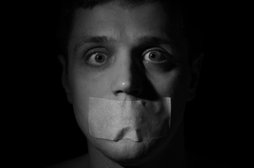 Face of a frightened man with a mouth taped violently with his mouth isolated on a black background