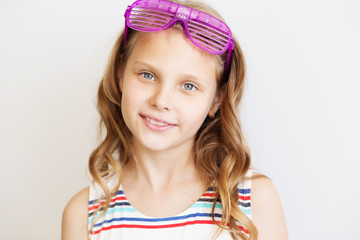 Lovely little girl in a striped dress with funny party plastic striped sunglasses in front of white background. Summer emotions