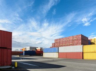 Dry cargo containers of different colors stacked in a shipping yard under a blue sky with white...