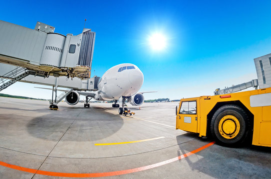 Parking at the airport, airplane at the teletrap. Aerodrome tractor is ready for towing and departure of the aircraft. Against the background of a blue sky and bright sun, nice weather.