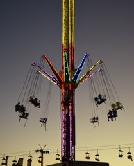 Carnival ride lit up at dusk, with people in swings up high.