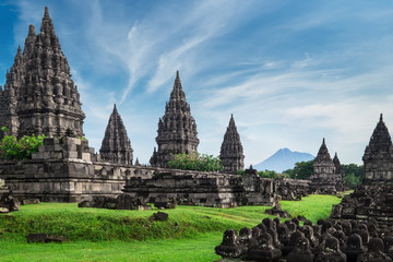 Ancient stone ruins on green field and Candi Prambanan or Rara Jonggrang, Hindu temple compound on background. Impressive architectural site. Yogyakarta, Central Java, Indonesia. Panoramic view.