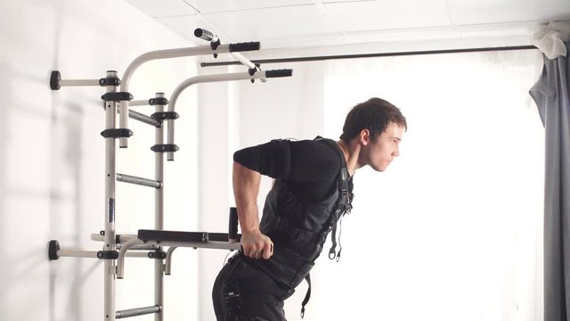 EMS. Fit man doing triceps dips on parallel bars.