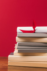 Cropped image of diploma on top of stack of books on red