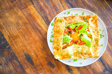 French pancakes crepes with egg and bacon. On a wooden table in the restaurant. The golden pancake crust is neatly wrapped in the filling: egg, bacon, lettuce leaves, tomatoes.Top view with copy space