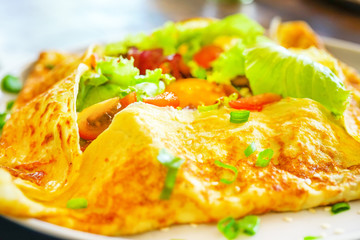 French pancakes crepes with egg and bacon. On a wooden table in the restaurant. The golden pancake crust is neatly wrapped in the filling: egg, bacon, lettuce leaves, tomatoes. Close view copy space
