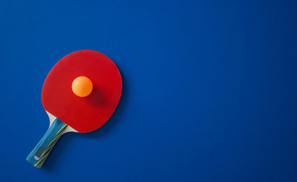 Red tennis racket lies on a blue table with a ball