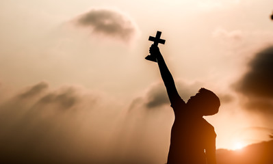 Young man holding christian cross and look up to sky with light sunset