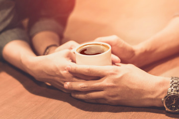 Fototapeta na wymiar hands of young lovers holding a hot cup of coffee