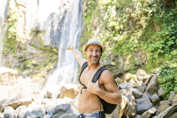 Attractive man standing by waterfalls on his back
