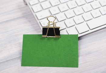 Business card in green color with golden clamp on computer keyboard. Mockup.