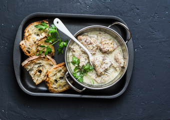 Mustard cream sauce stewed pork and grilled bread - delicious lunch on dark background, top view. Flat lay