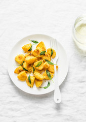 Crispy polenta crust potatoes baked with sage butter and a glass of white wine on a light background, top view
