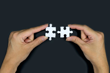 Female hand holding a white jigsaw on a black background. Business connection concept.