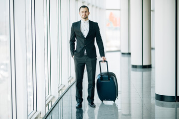 Businessman dragging a small carry on luggage suitcase at airport corridor walking to departure gates. Business trip