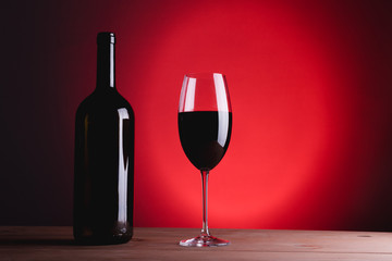 bottle of wine and glass with red wine, on red background, copy space