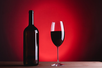 bottle of wine and glass with red wine, on red background, copy space