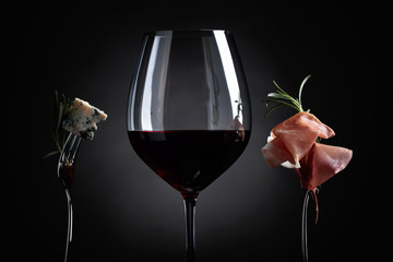 Glass of red wine with blue cheese and prosciutto .