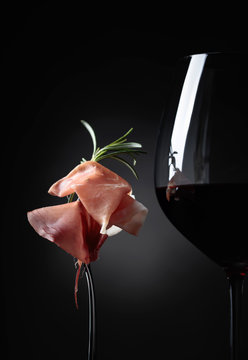 Glass of red wine with prosciutto and rosemary.