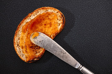 one toast with apple jam and knife on black background. Top view