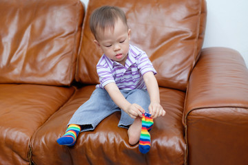Cute little Asian 18 months / 1 year old toddler boy child sitting on sofa in living room...
