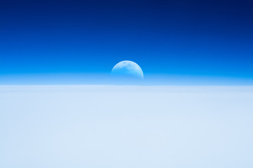 Half Moon rising from the Earth horizon above the clouds.