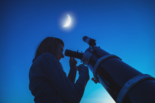 Silhouette of a girl and telescope with Moon on the sky. 