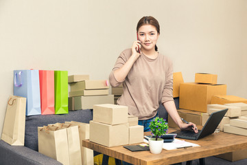 Young happy asian online seller, business woman, in her home talking to her customer on her phone while looking at camera