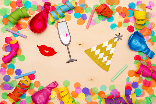 Colorful confetti, streamer and party hat on wooden background from above