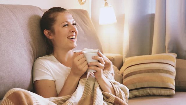Young female is watching TV and sitting with tea at home.