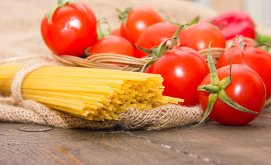 long pasta and ripe red cherry tomatoes on a wooden brown table on a beige bag