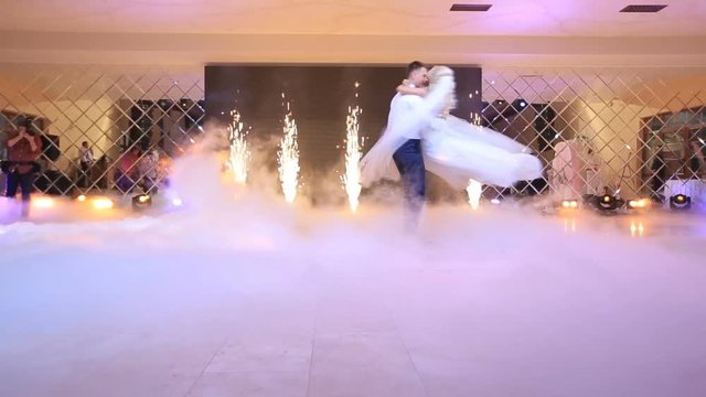 Amazing first dance of happy newlyweds. The groom is spinning his beautiful bride while being shouded by white fume at the background of the cold fireworks in the restaurant.