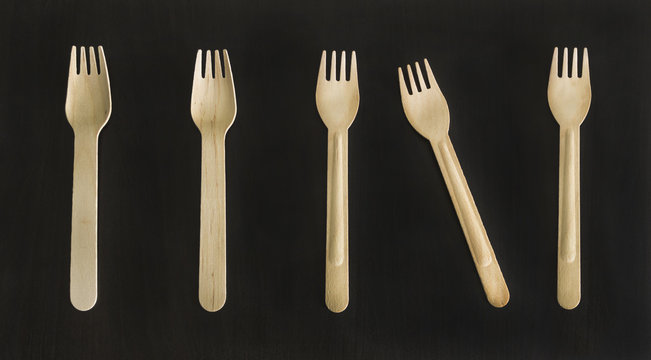 Disposable wooden ecologically designed forks and spoons for takeout meal, food to-go on the black background. Conceptual.