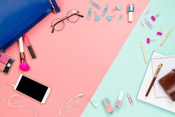 Business frame flatlay with woman's blue bag, glasses, smartphone with black copyspace, cosmetics and stationary supples. Pastel pink and mint background, business mockup, women work bag contents