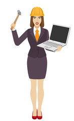 Businesswoman in construction helmet trying to break a laptop notebook with a hammer