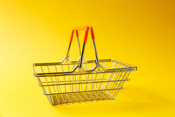 Close up of metal grocery basket for shopping in supermarket with raised handles and orange plastic elements isolated on yellow background. Concept of shopping. Copy space for advertisement